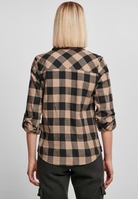 Chemise à carreaux marron et noir avec des manches retroussées ; tissu doux, ourlet arrondi, détail de l'empiècement d'épaule et couture visible. Vue de dos.