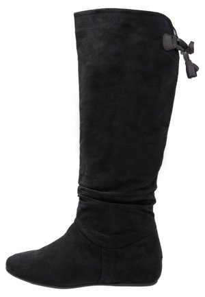 Czarny, zamszowy, płaski kozak za kolano z miękką cholewką, ozdobną kokardą z tyłu, zaokrąglonym noskiem i niskim obcasem.