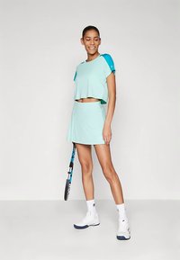 Et sportsantrekk i mintgrønt med en kort genser med korte ermer og et matchende plissert skjørt. Brukes med hvite treningssko.