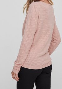 Pull rose clair avec un motif texturé en nid d'abeille. Il présente des manches longues et un col rond, avec des poignets et un ourlet côtelés.