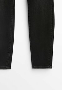 Partie inférieure d'un jean noir slim avec coutures visibles sur fond blanc.