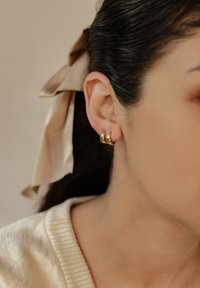 Boucles d'oreilles en or en forme de cercle avec un design courbé, présentant une finition polie. Portées sur le lobe de l'oreille, elles mettent en valeur leur style épuré et minimaliste.