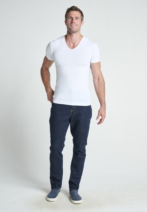 Camiseta blanca ajustada de cuello en V, de mangas cortas, combinada con pantalones vaqueros de mezclilla azul oscuro y zapatos de lona azules. Diseño simple, textura suave.