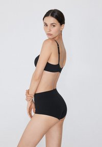 Schwarzes Unterwäsche-Set mit einem nahtlosen Bralette mit verstellbaren Trägern und hochgeschnittenen Shorts. Glatte Textur, minimalistisches Design.