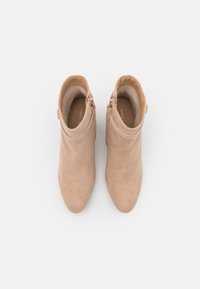 Bottes chevilles beige en daim, avec une texture lisse, un bout pointu et une fermeture éclair latérale avec des garnitures dorées.