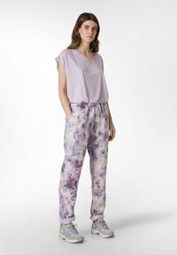 Lichtpaarse top met korte mouwen, gecombineerd met loszittende, taille-touwbroek met een bloemenpatroon in paars en opgerolde manchet. Grijze sneakers.