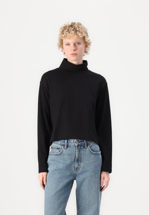 Svart langermet topp med høy hals, laget av mykt stoff, sammen med lyseblå høytaljede jeans med klassisk fem-lomme design.
