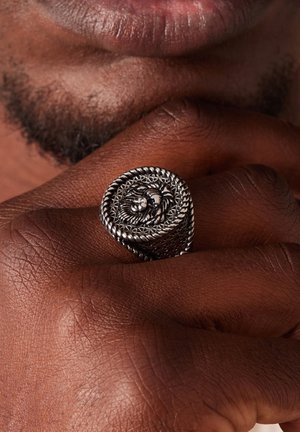 Sterling zilveren ring met een leeuwontwerp, met ingewikkelde filigraan details en een gedraaide band. Tegen een donkere huidtoon.