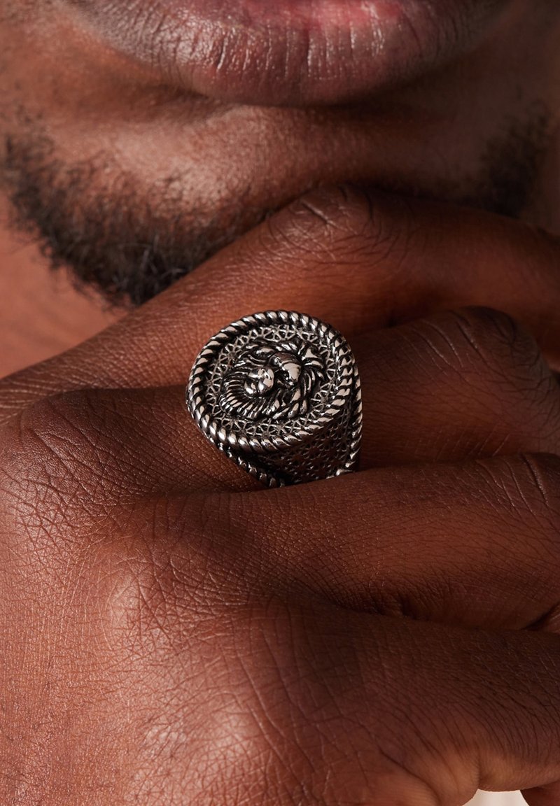 Sterling zilveren ring met een leeuwontwerp, met ingewikkelde filigraan details en een gedraaide band. Tegen een donkere huidtoon.