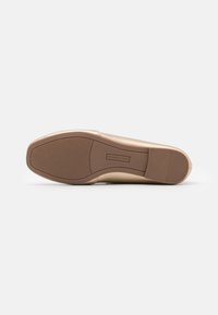 Beige eskaat jalkine pyöreällä varvaskärjellä ja sileällä nahkapinnalla. Teksturoidulla kumipohjalla on va Horizontal grooves, jotka tarjoavat pitoa. Minimalistinen muotoilu.