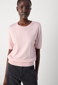Light pink short-sleeved sweater with a round neckline, ribbed cuffs and hem, crafted from a soft texture. Paired with dark gray pants.