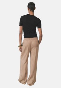 Black fitted t-shirt paired with loose, light beige linen trousers, featuring an elastic waistband and a textured finish.