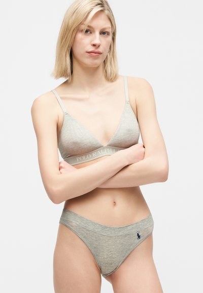Γυναίκα με ξανθά μαλλιά που φοράει ανοιχτό γκρι σουτιέν Polo Ralph Lauren και ταιριαστό εσώρουχο, στέκεται με τα χέρια σταυρωμένα μπροστά σε λευκό φόντο.