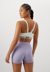 Hvit sports-bh med svart "Nike" logo-bånd, kombinert med lyse lilla høytlivshorts som har en liten logo på baksiden.