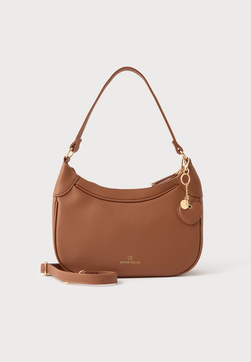 Sac à main en cuir grainé marron avec une forme incurvée, des accents de quincaillerie dorée, une bandoulière amovible et un petit charme, arborant le logo de la marque.