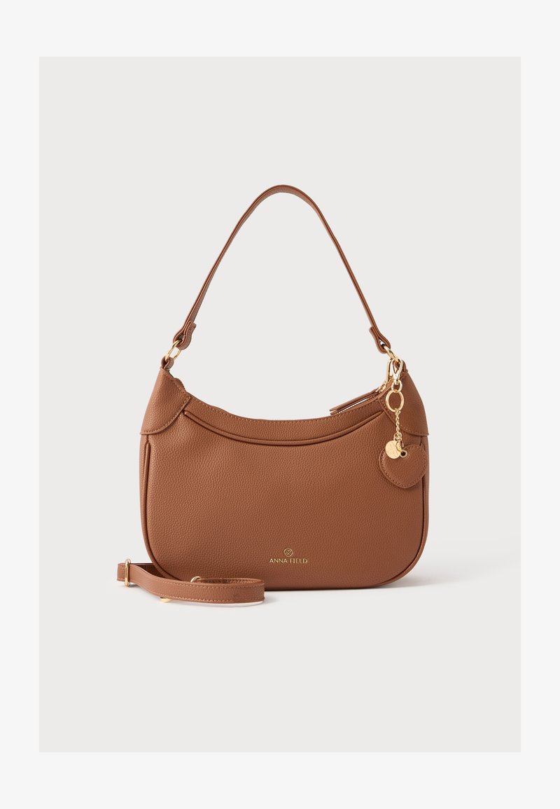 Sac à main en cuir grainé marron avec une forme incurvée, des accents de quincaillerie dorée, une bandoulière amovible et un petit charme, arborant le logo de la marque.