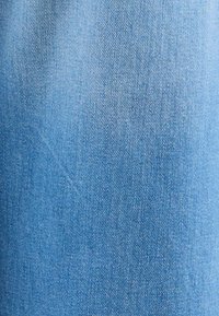 Gros plan sur un tissu en denim bleu clair montrant une texture de tissage diagonal détaillée et des variations de couleur subtiles.