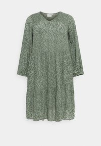 Zielona sukienka w kwiatowy wzór, z dekoltem w kształcie litery V, długimi rękawami i warstwowym krojem. Wykonana z lekkiego materiału z delikatnym nadrukiem kwiatowym.