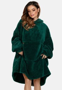 Coperta con cappuccio oversize di colore verde, realizzata in morbido materiale in pile, con una ampia tasca frontale e un orlo curvo per un comfort aggiuntivo.