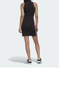 Černé bezrukávové šaty s vysokým límcem; mají červené a modré boční pruhy; střih je přiléhavý; nošeny s černobílými teniskami.