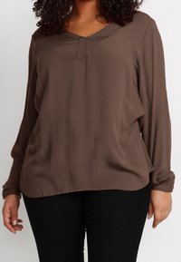 T-shirt marron à manches longues en tissu texturé avec un décolleté en V et un détail de bouton à l'avant. Associé à un pantalon noir.