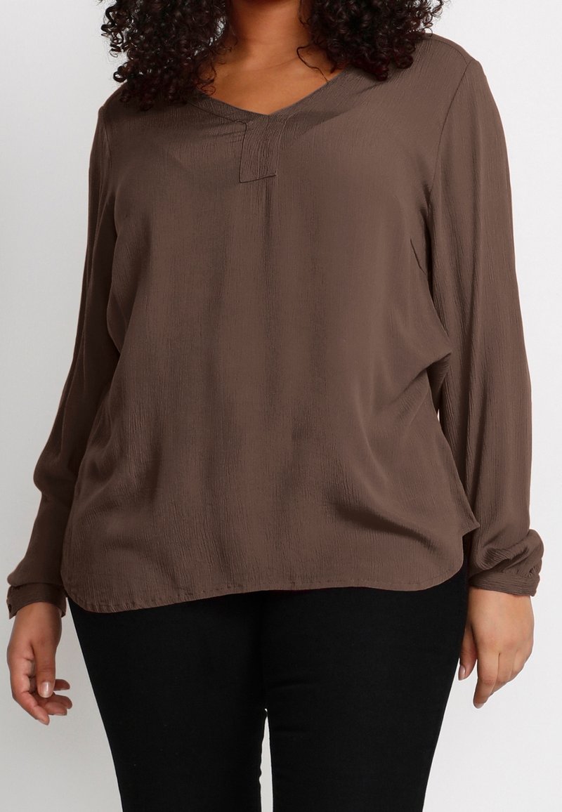 T-shirt marron à manches longues en tissu texturé avec un décolleté en V et un détail de bouton à l'avant. Associé à un pantalon noir.