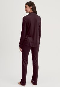 Bordeaux pyjama set met een lange mouw top en broek, voorzien van witte biezen langs de kraag en manchetten, gemaakt van zachte stof.
