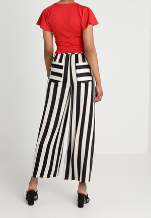 Punainen lyhythihainen yläosa, jossa on vartalonmyötäinen malli, yhdistettynä leveälahkeisiin mustavalkoraidallisiin housuihin, joissa on kaksi takataskua ja sileä pinta.