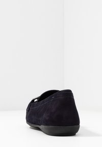 Navyblauer Wildlederschuh mit niedrigem Profil, strukturierten Oberflächen, abgerundetem Zeh und schwarzer Gummisohle. Verfügt über ein dezentes Metallelement.