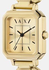 Goldfarbene quadratische Armbanduhr mit schwarzen Stundenmarkierungen, schwarzen Zeigern und den Buchstaben A und X auf der 12-Uhr-Position an einem Gliederarmband.