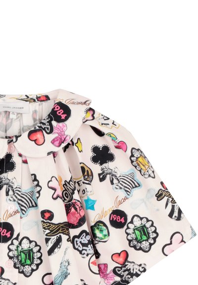 Kinderhemd mit bunten grafischen Aufnähern, darunter Herzen, Schleifen, Sterne, Edelsteine, die Jahreszahl "1984" und der Schriftzug "Marc Jacobs" auf hellem Stoff.