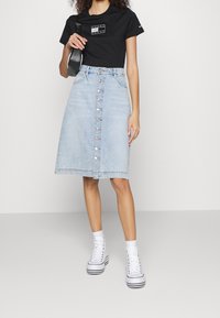 Džínová áčková sukně ve světle modré barvě s předním zapínáním na knoflíky, kombinovaná s černým grafickým tričkem a bílými vysokými teniskami.