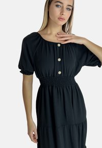 Abito nero leggero con maniche corte a palloncino, vita smock e tre bottoni. Presenta un design a gonna a strati fluente.