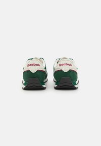 Zeleni i bijeli tenisice od antilopa. Imaju Reebok logo u ružičastoj boji na peti i crnu gumu s teksturiranim uzorkom.