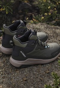 Green and black Terrex hiking shoes with padded ankle collar on gravel surface outdoors.