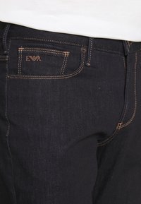 Mörkblå denimjeans med låg midja, featuring orange sömmar och en liten präglad logotyp på bakfickan.