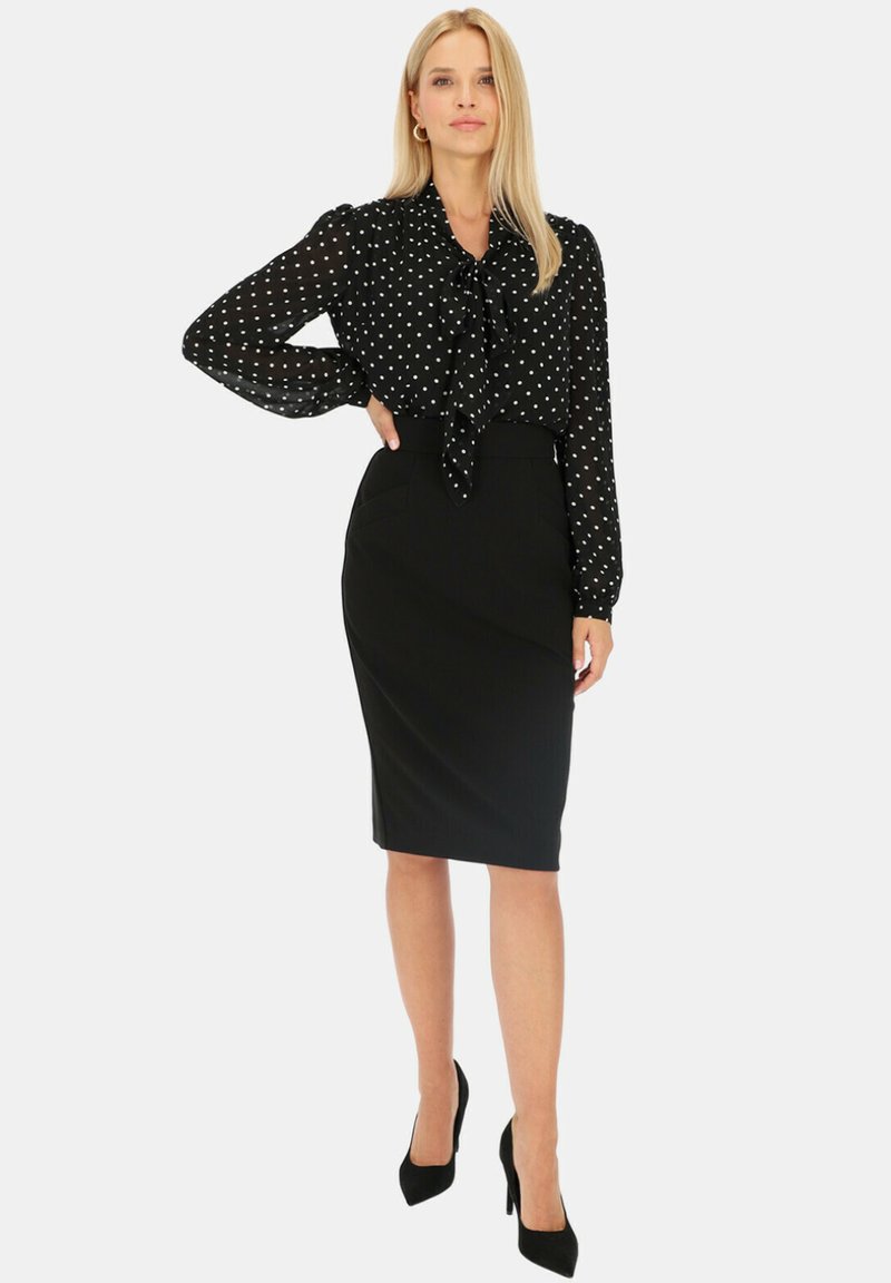 Czarna bluzka w białe kropki, zawiązywanie przy dekolcie, długie rękawy. Dopasowana czarna spódnica ołówkowa, gładka faktura, długość powyżej kolan.