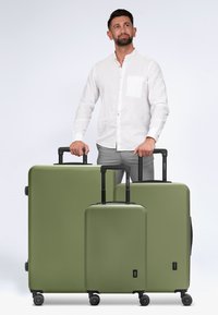 Drie groene harde koffers in verschillende maten met zwarte hardware, telescopische handgrepen en vier wielen voor mobiliteit.