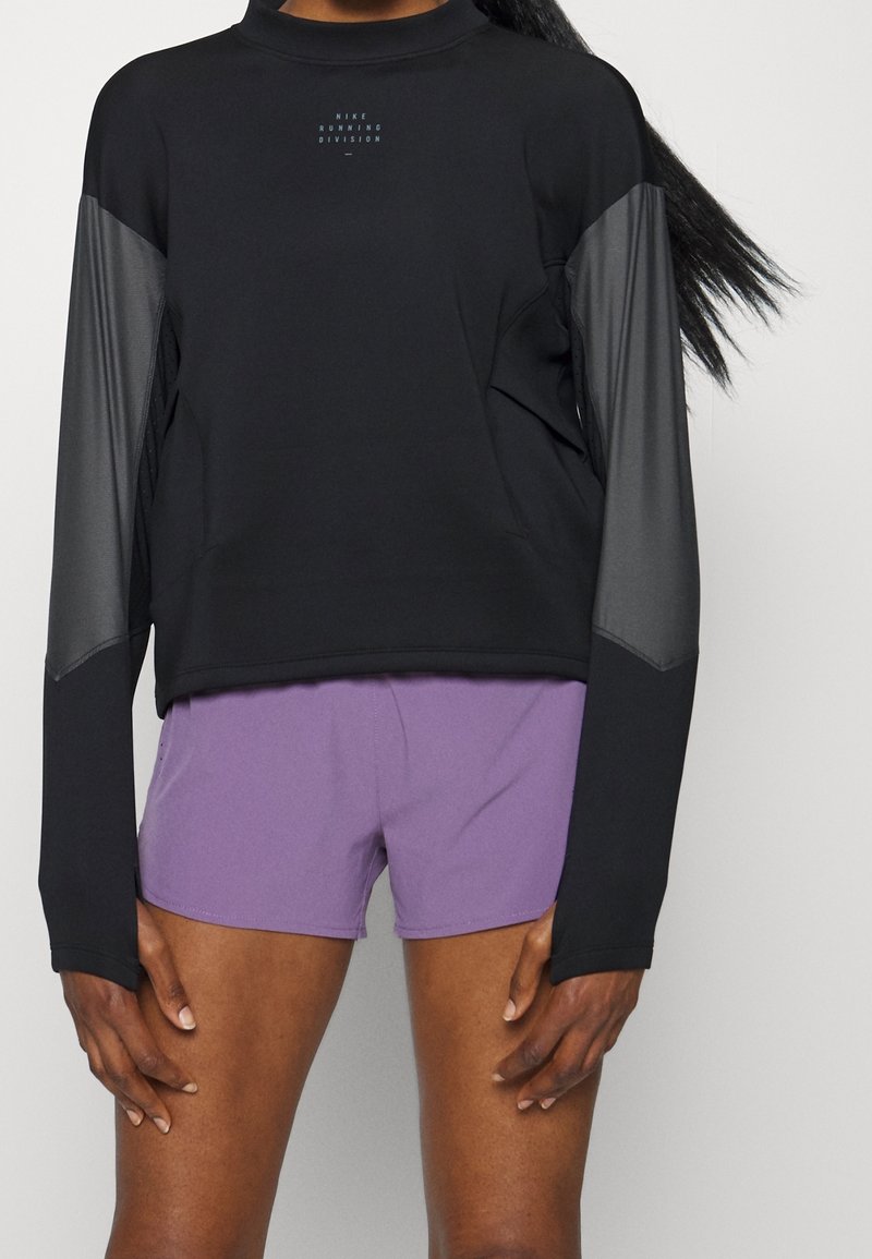 Maglia da corsa nera a maniche lunghe con accenti in rete grigia e logo, abbinata a pantaloni corti viola; presenta un design aderente e una texture liscia.