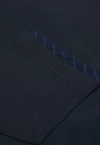 Námořnická bavlněná tkanina s kapsou na hrudi a modrým pruhovaným vzorem. Hladká textura s viditelným prošíváním kolem kapsy.