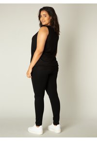 Zwarte mouwloze top en zwarte leggings, beide in een aansluitend ontwerp. Model draagt witte sneakers. Gladde stof zonder zichtbare patronen.