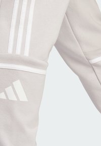 Lys grå sweatshirt med hvide detaljer, der har tre lodrette striber på ærmet og et hvidt logo nederst. Blød tekstur.