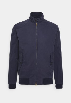 Granatowa kurtka na zamek z wysokim kołnierzem, zapięciem na zatrzaski przy szyi, dwoma zapinanymi na guziki kieszeniami bocznymi oraz ściągaczami na mankietach i dole.