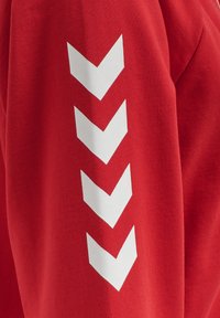 Rode stof met een verticale rij van vier witte naar beneden wijzende chevronvormen gedrukt op het oppervlak.