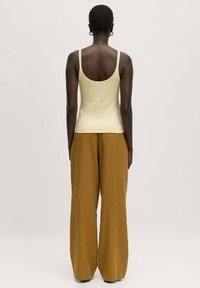 Geel geribbeld tanktop met dunne bandjes, gecombineerd met hoge taille, wijde bruine broek, gezien vanaf de achterkant. Soepele textuur, minimalistisch ontwerp.