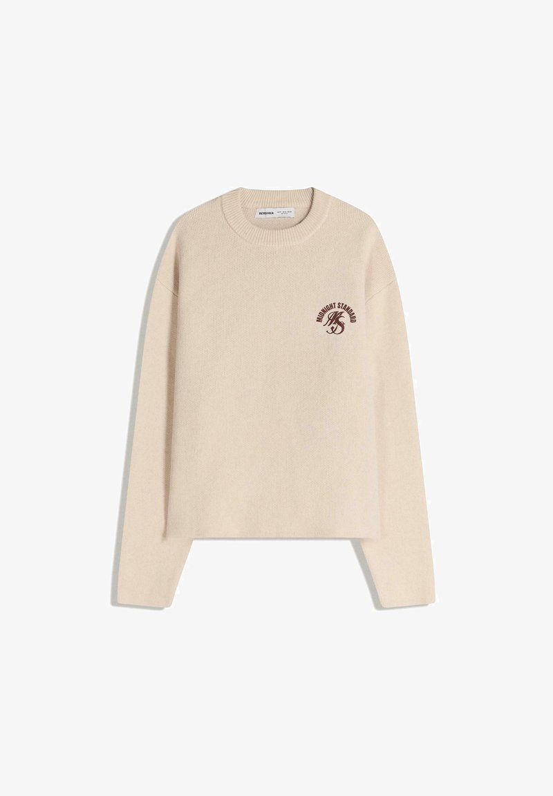 Béžový pletený svetr s kulatým výstřihem, spadlými rameny a malým vínovým logem na levé straně. Zkrácená délka.