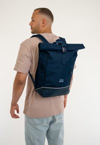 Tengerészeti roll-top hátizsák tartós anyagból készült. Elülső cipzáras zsebbe, állítható pántokra és fényvisszaverő alsó díszítésre is jellemző.