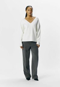 Witte, lange mouwen trui met een diepe V-hals, gecombineerd met grijze, wijde broek. Soepele textuur, minimalistisch ontwerp en op maat gemaakte pasvorm.
