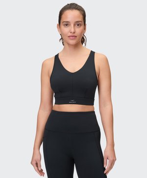 Woman wearing a black sports bra and high-waisted leggings standing against a light gray background, facing forward.