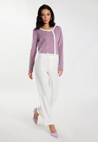 Lavendel cardigan met witte bies en knopen, gecombineerd met witte wijde broek en lila hoge hakken, op een neutrale achtergrond.